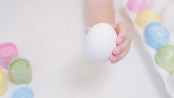 Macro a Child's Hand Holds a White Chicken Egg and Begins to Paint It Yellow