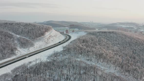 Approach of a Drone From the Road with Traffic Among the Hills in Winter