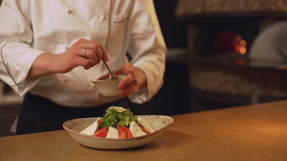 Chef Cook Decorate Tomato and Cheese Salad with Sausce on Wooden Table in Slowmotion