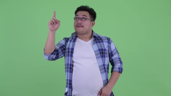 Happy Young Overweight Asian Hipster Man Pointing Up