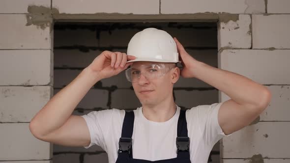 A Male Worker Puts on a White Construction Helmet on a Construction Site