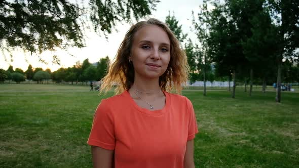 Portrait of a Smiling Blonde in a Sports T-shirt in the Park on a Sunset Background, Slow Motion