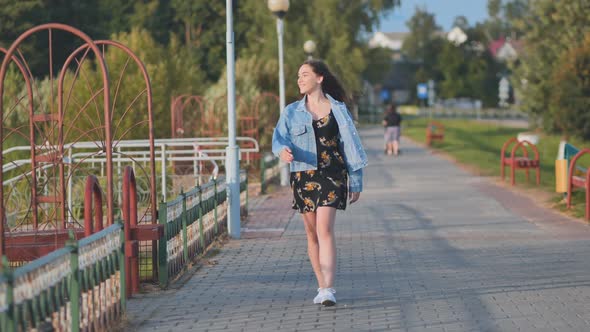 A Cheerful Girl Walks Along the City Promenade