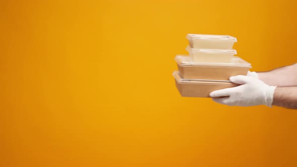 People's Hands Passing Each Other Packed Boxes with Food Delivery Against Yellow Studio Background