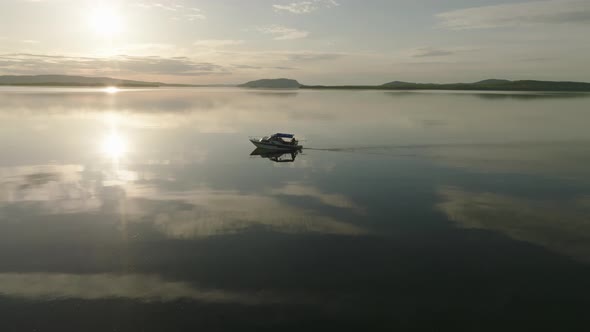 A boat silhouetted against sunset crossing flat calm lake