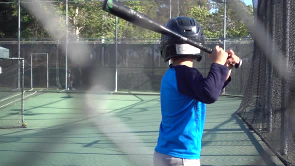 A boy practices baseball at a batting cage.