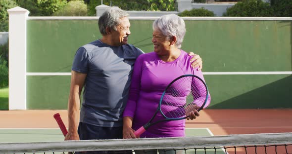 Video of happy biracial senior couple holding rackets on tennis court