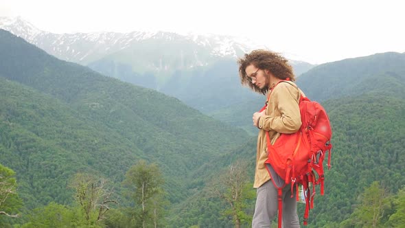 Man Traveler with Red Backpack Looking at Camera Outdoor with Rocky Mountains on Background