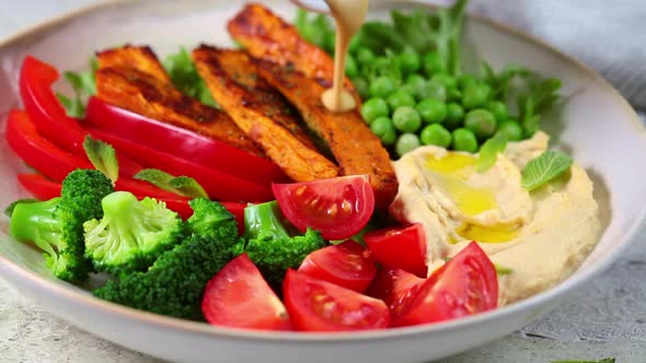 Cooking vegan salad bowl with sweet potatoes, broccoli, tomato and hummus