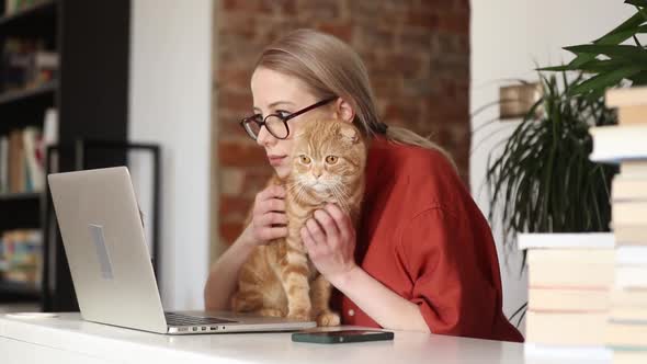 beautiful woman sitting at table with a ginger cat and working in her home office