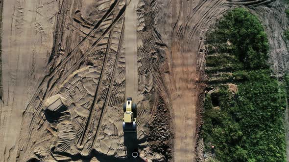 An overhead view of a yellow road roller moving across a sandy construction site