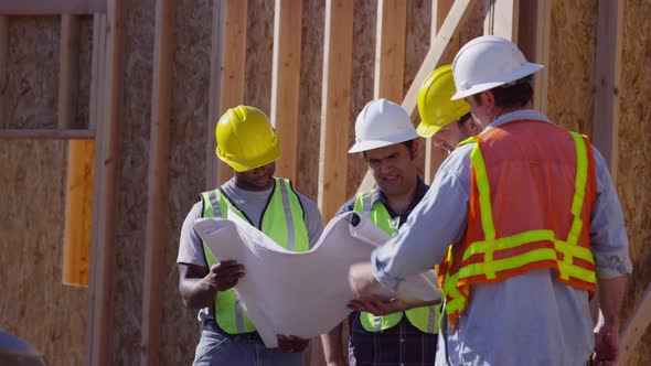 Group of construction workers look at plans alt