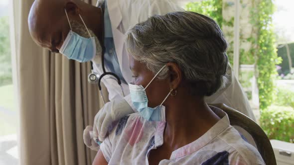 African american senior male doctor injecting covid-19 vaccine into african american woman at home