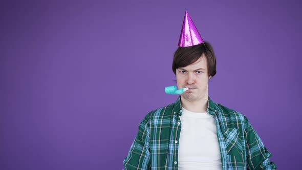 Young Man in Birthday Cone Cap Blowing Squeaker Frowns