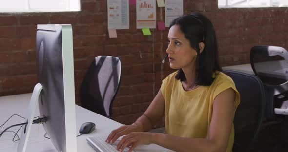 Mixed race businesswoman wearing headset sitting at desk using computer