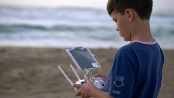 Boy Operating a Drone with Remote Control. Quadrocopter Drone Flying Over Sunset Sea