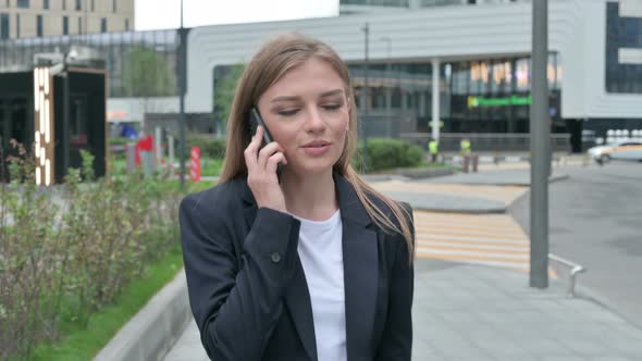 Happy Businesswoman Attending Phone Call While Walking on the Street