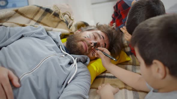 Mischievous Boys Painting Face of Father Sleeping on Couch at Home