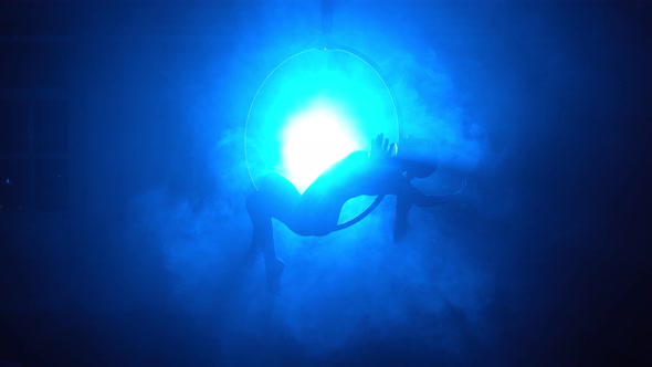 Silhouette Aerial Gymnast Performs Trick in Ring in Smoky Room with Backlit