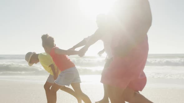 Smiling senior african american couple running with grandchildren on sunny beach