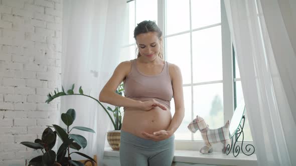 Closeup Smiling Belly Mother Thinking About Future Baby Near Window at Home.