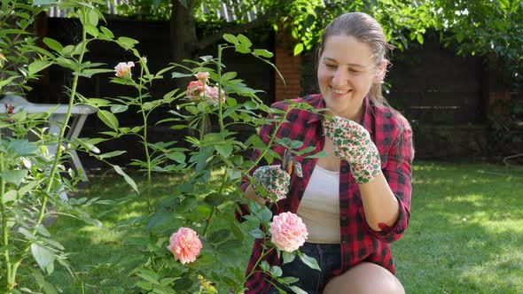 Beautiful Smiling Woman in Gloves Taking Care of Blooming Roses in Garden at House Backyard