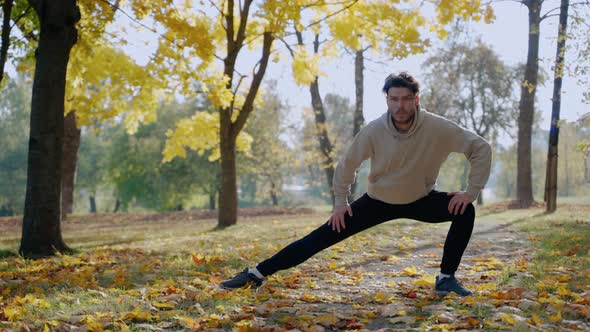 Man Exercising and Stretching Before Morning Run at the Park in Autumn