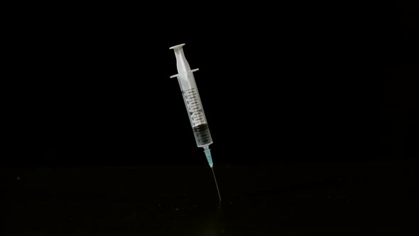 Syringe falling and sticking on black background, Ultra Slow Motion