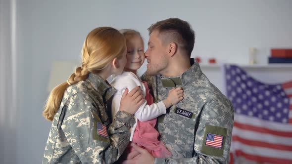 Cheerful Military Couple Kissing Little Child in Cheeks, USA Flag on Background