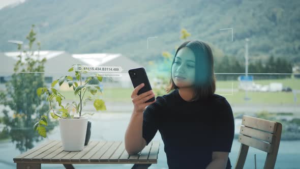 Young woman at table outside use smartphone device for digital biometric facial recognition, pattern