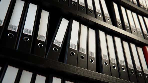 Close up on the row of the file black binders stacked on the wooden shelf.