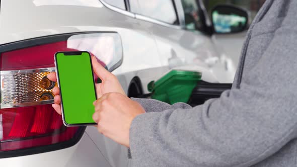 Woman Uses a Mobile Application in a Smartphone To Pay for Refueling a Car. Smartphone with a Green