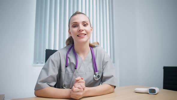 Woman Doctor Sits at Workplace Looks at the Camera and Communicates with the Patient Via Video Call