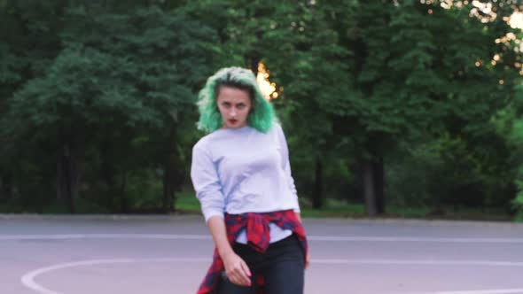 Young Stylish Funky Girl with Green Hair Riding Roller Skates and Dancing in Park Slow Motion