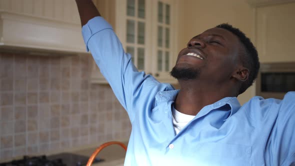 Excited Satisfied Young Man Stretching Hands Standing in Kitchen at Home Indoors