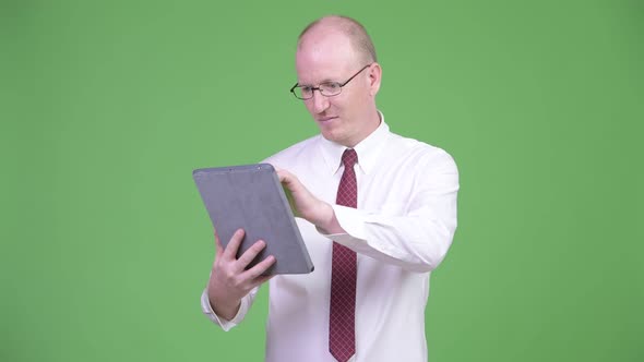 Happy Mature Bald Businessman Using Digital Tablet and Looking Shocked
