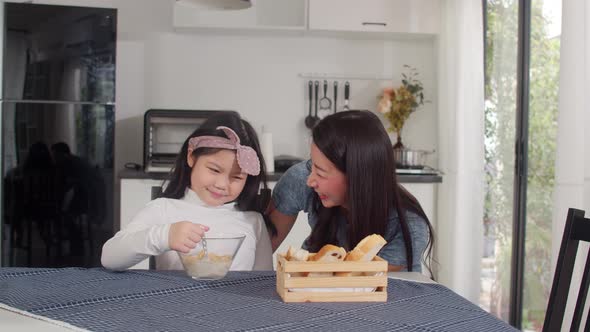Asian mom and daughter feeling happy talking together while eat bread, corn flakes.