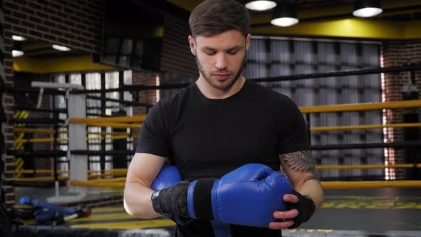 Young Muscular Male Boxer Puts on Boxing Gloves in the Gym