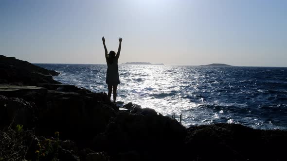 Slender Blonde in Striped Dress Stands Against Backdrop of Sea or Ocean and Looks Into Distance