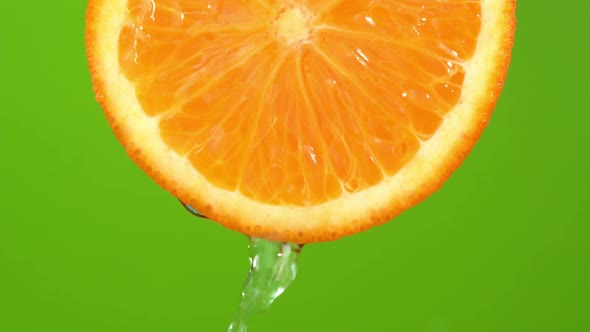 Water falling from orange hue orange on green background. Orange slice and water splashing, drops