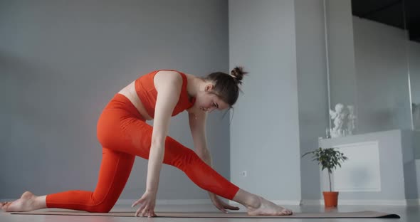 Young Woman in Red Tracksuit Sitting on the Yoga Mat and Leaning Forward To Her Feet, Person Does