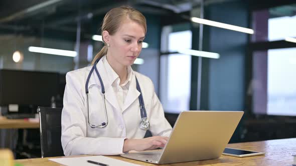 Cheerful Young Female Doctor Working on Laptop in Office