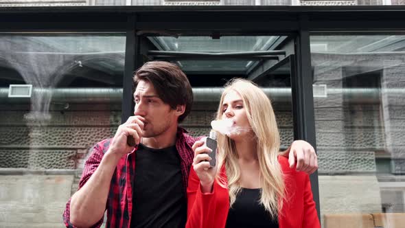 Stylish Couple in a City. Two People Use the Electronic Cigarette