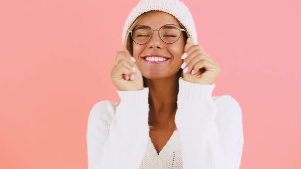 Young Female in Glasses White Jumper and Knitted Hat is Dancing and Laughing While Posing Against