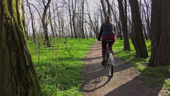 Young Woman on a Bicycle Rides Along a Path in the Forest in a Sunny Spring Day