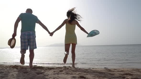 Active Couple Running on a Yellow Sandy Beach with Blue Sky and Sea on the Background