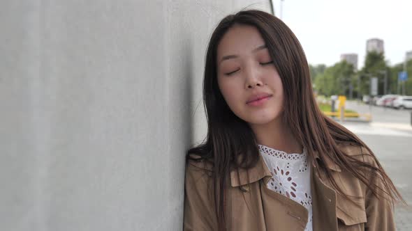 A Young Woman Poses for the Camera Leaning Against a Grey Wall in the Street