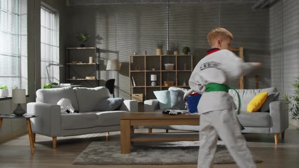 Karate Boy in White Kimono Trains at Home in the Living Room
