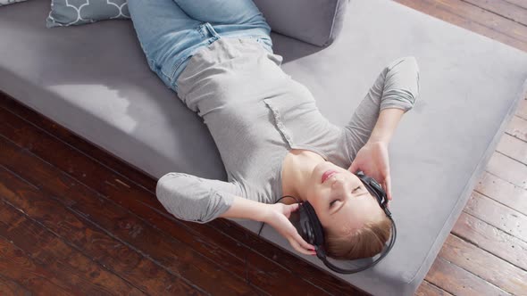 Young beautiful girl lies on a sofa in headphones