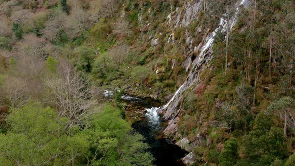 Rio Sor at the bottom of the rocky valley with a violent waterfall falling from the summit. Drone fi